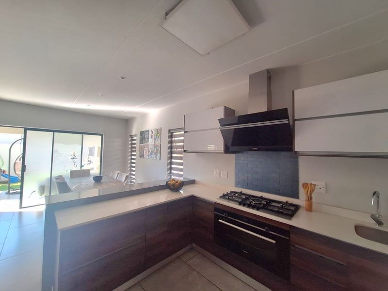 Modern open-plan kitchen featuring dark wood cabinetry, stone countertops, gas hob, and integrated appliances, flowing seamlessly into the dining area with sliding door access.