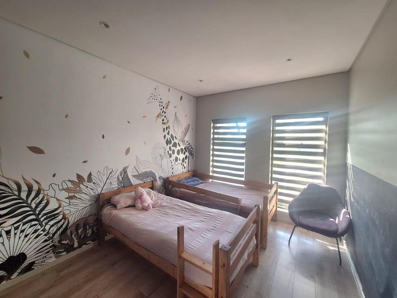 A well-maintained bedroom featuring laminate flooring, recessed downlights, and modern roller blinds, accented by a decorative feature wall.