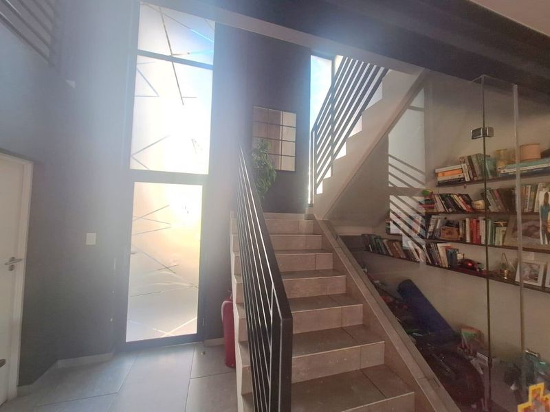 Modern entrance hall featuring a tiled staircase with metal balustrades, high ceilings, and large glass panels providing ample natural light.