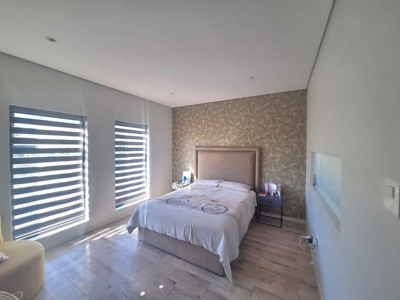 A well-maintained bedroom featuring modern laminate flooring, recessed lighting, and a stylish patterned feature wall with dual roller blinds.