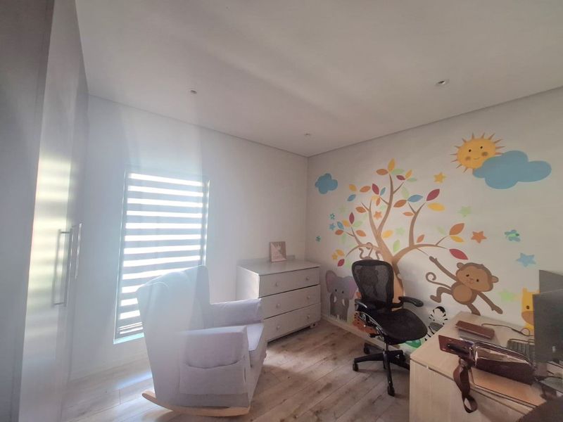 A bright bedroom featuring laminate flooring, built-in cupboards, and recessed downlights, currently utilized as a nursery and home office space.
