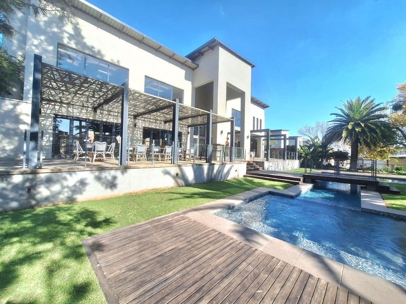 Spacious rear exterior featuring a modern swimming pool, timber decking, decorative pergola, and a pedestrian bridge leading to a landscaped garden area.