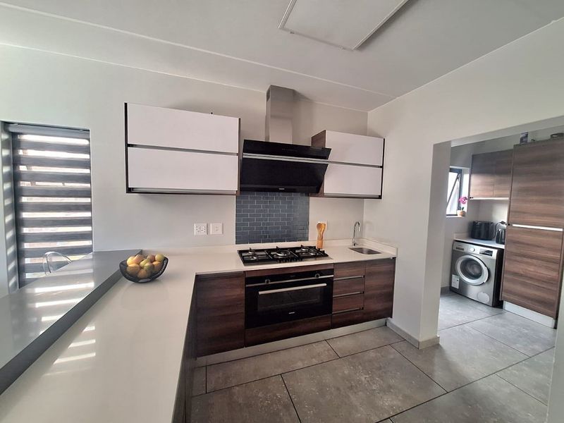 Modern kitchen featuring sleek wood-tone cabinetry, stone countertops, a gas hob with extractor, and a subway tile backsplash, with an adjacent scullery area.