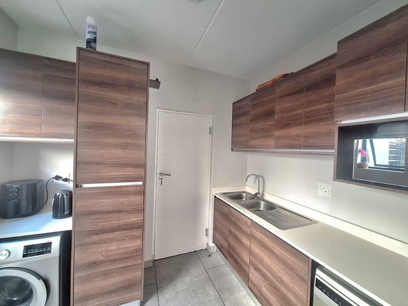 A functional scullery featuring modern wood-look cabinetry, stainless steel sink, integrated microwave, and tiled flooring, providing efficient additional workspace and storage.