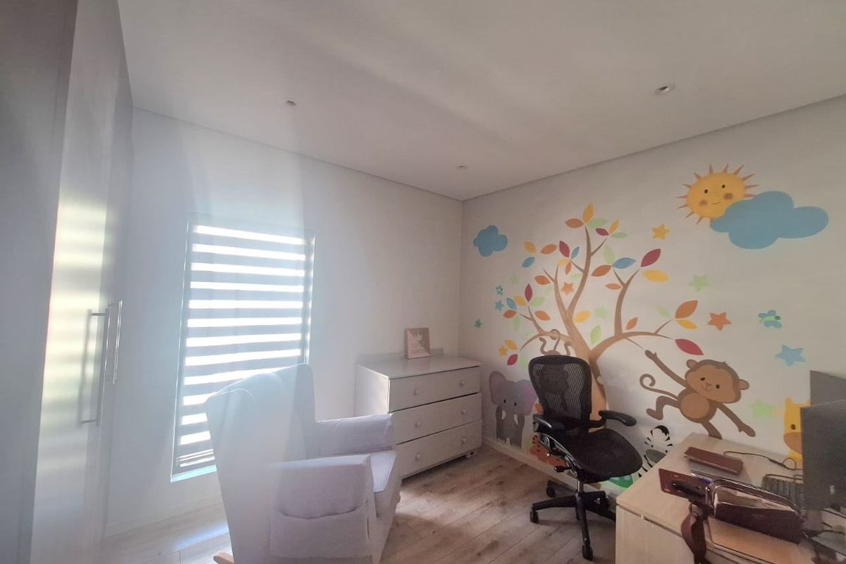 A bright bedroom featuring laminate flooring, built-in cupboards, and recessed downlights, currently utilized as a nursery and home office space.