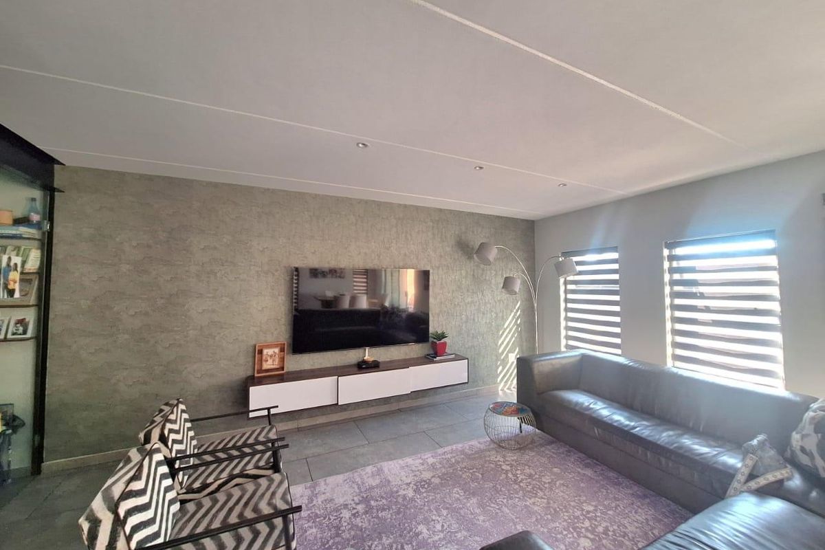 A modern living room featuring a textured feature wall, floating media console, tiled flooring, and recessed downlights with natural light from dual windows.