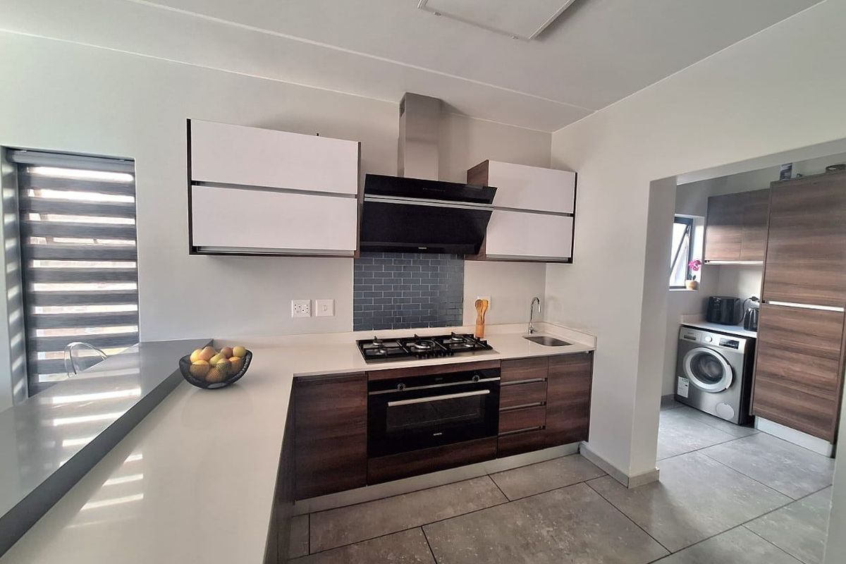 Modern kitchen featuring sleek wood-tone cabinetry, stone countertops, a gas hob with extractor, and a subway tile backsplash, with an adjacent scullery area.