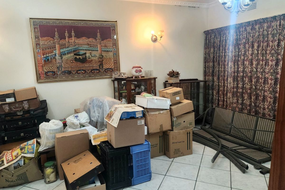 A living room area featuring tiled flooring, decorative ceiling cornices, and traditional lighting fixtures, currently used for storage.