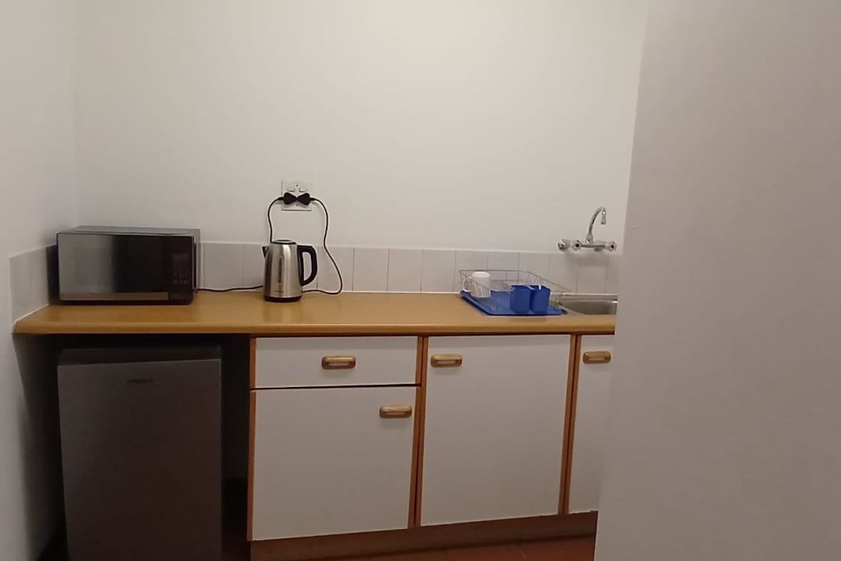 A compact kitchenette featuring laminate countertops, built-in cabinetry, a stainless steel sink, and a tiled splashback.