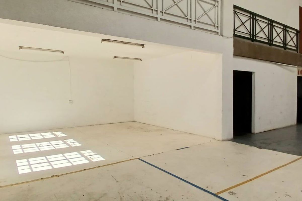 Spacious industrial utility area featuring concrete flooring, a mezzanine level with metal railings, and a large roller shutter door for easy access.