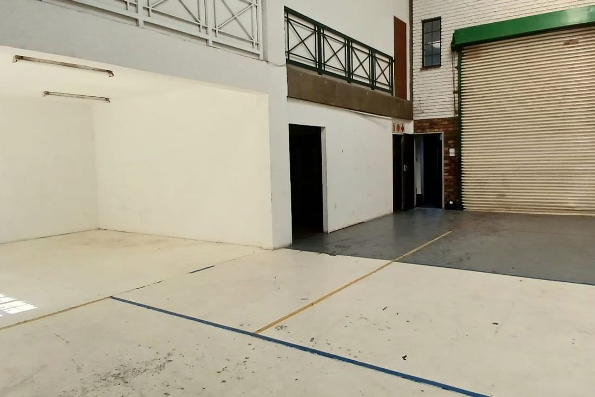 Spacious industrial garage area featuring a large roller shutter door, mezzanine level with metal railings, and durable painted concrete flooring.
