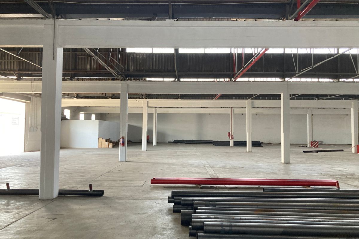 Spacious industrial warehouse featuring high ceilings, exposed steel roof trusses, concrete flooring, and an integrated fire sprinkler system.