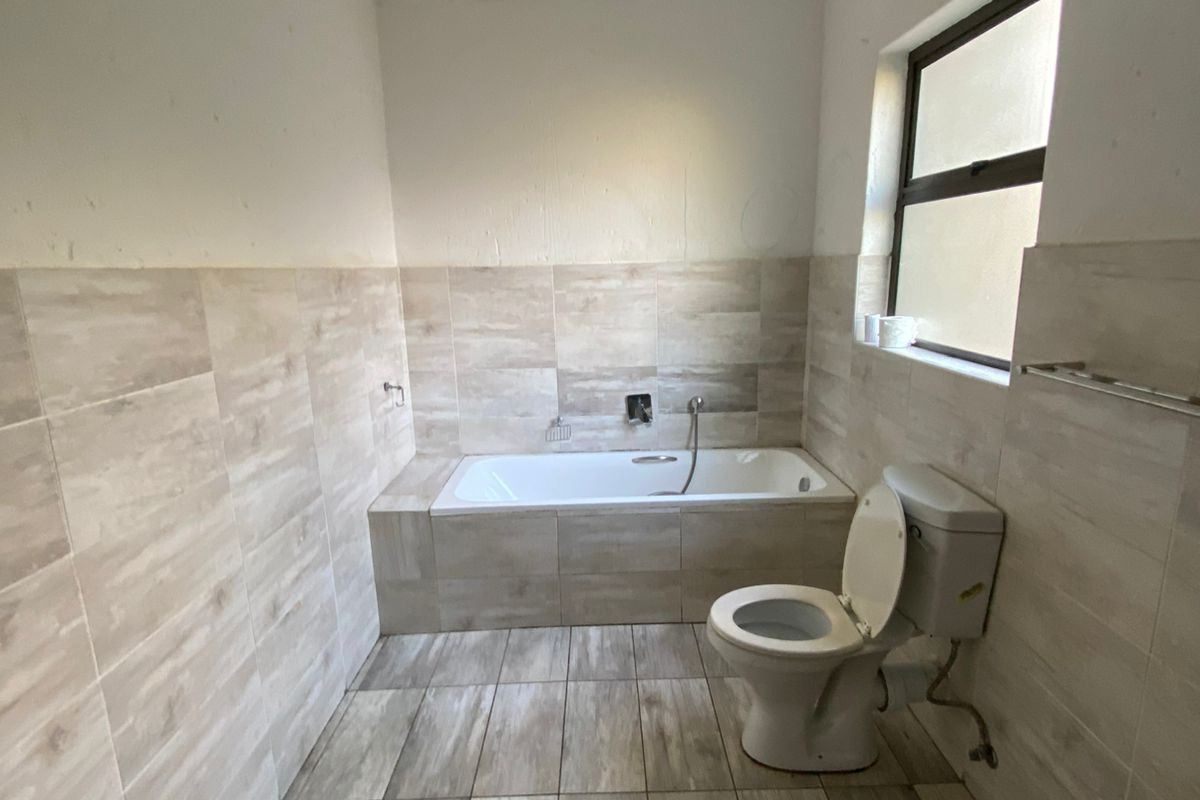 A functional bathroom featuring a built-in bathtub, toilet, and neutral wood-look floor and wall tiling.