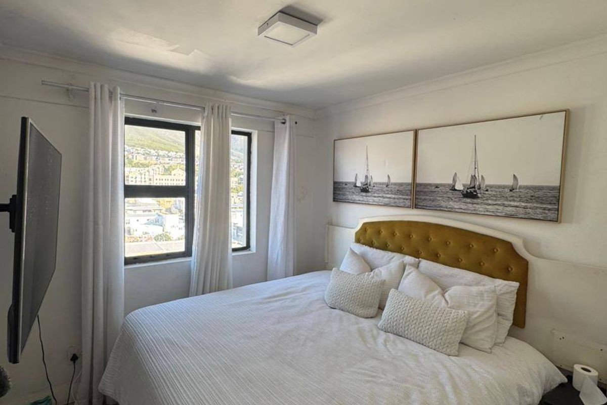 A well-maintained bedroom featuring neutral walls, light-toned flooring, and a window providing natural light and urban views.