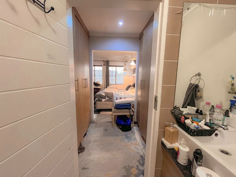 A hallway connecting a bathroom vanity area to a bedroom, featuring built-in cupboards and tiled flooring.