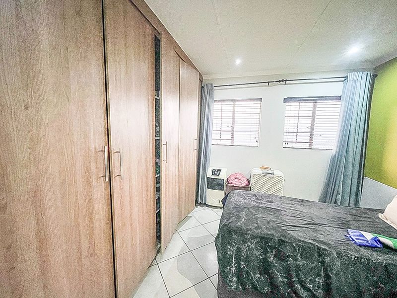 Bedroom featuring extensive built-in wooden cupboards, tiled flooring, and dual windows with venetian blinds, providing ample storage and natural light.