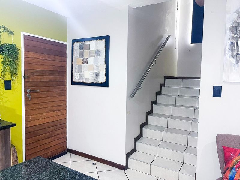 Entrance area featuring a solid wood front door, tiled staircase with a modern stainless steel handrail, and neutral ceramic floor tiling.