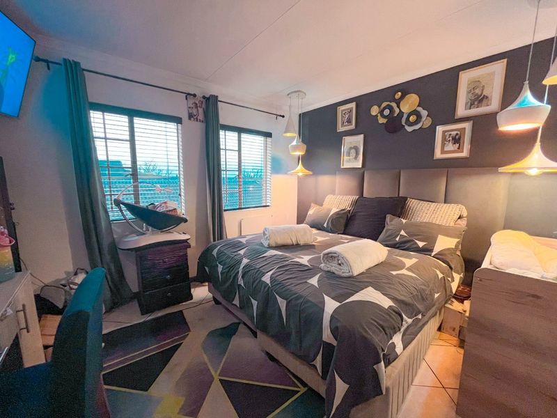 A well-lit bedroom featuring tiled flooring, venetian blinds, and a modern upholstered headboard with integrated pendant lighting.