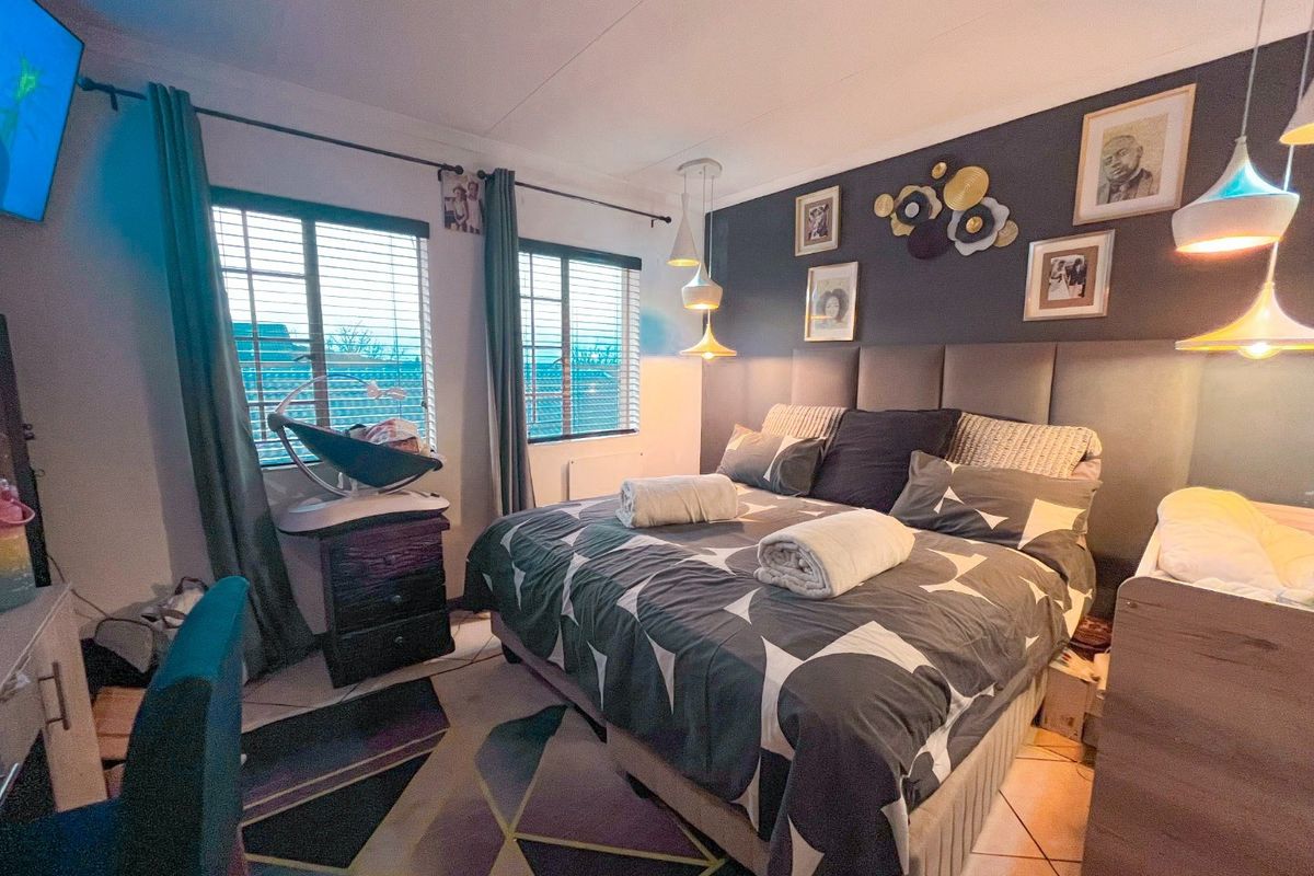 A well-lit bedroom featuring tiled flooring, venetian blinds, and a modern upholstered headboard with integrated pendant lighting.