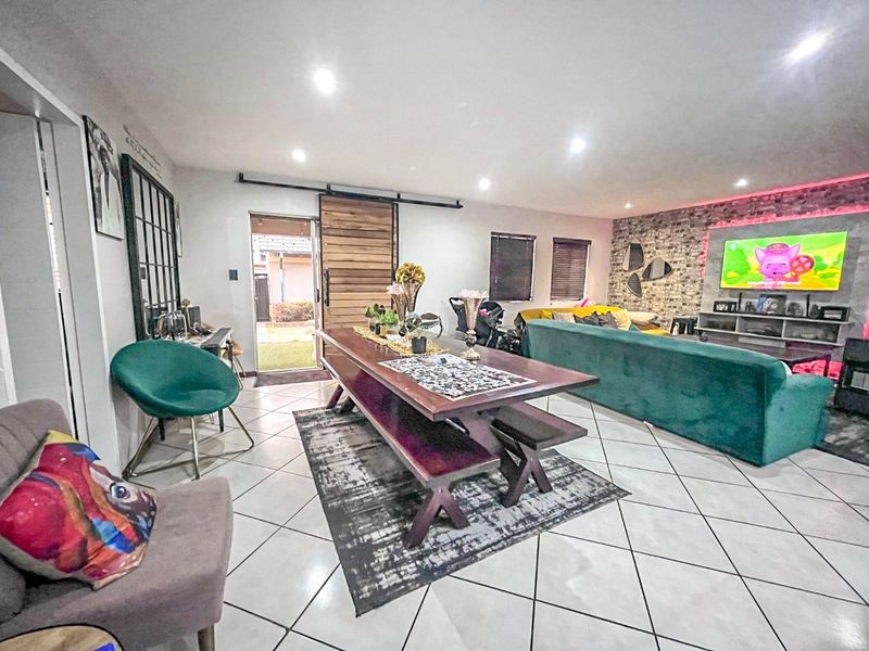 Spacious open-plan living and dining area featuring tiled floors, recessed lighting, and a distinctive exposed brick feature wall with a sliding barn door entrance.