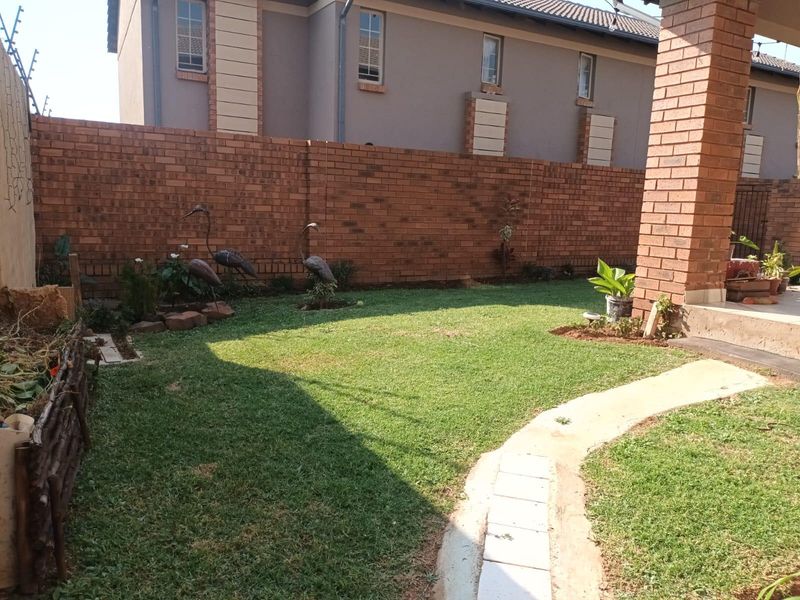 A private rear garden featuring a well-maintained lawn, a brick boundary wall, and a paved walkway leading to a covered patio area.