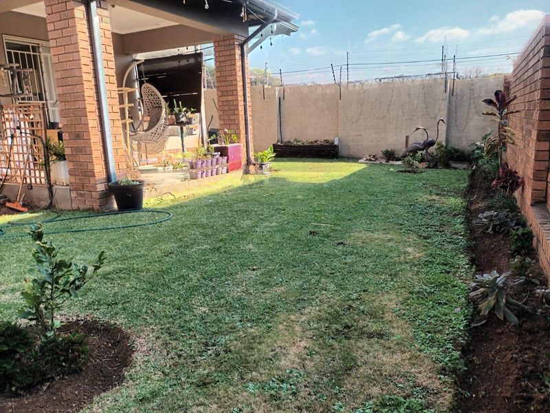 A private rear garden featuring a covered brick patio, established lawn, and secure perimeter walling with electric fencing.