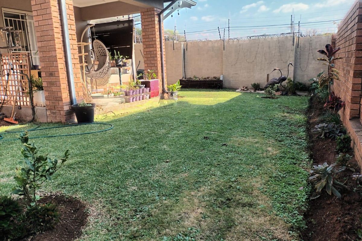 A private rear garden featuring a covered brick patio, established lawn, and secure perimeter walling with electric fencing.