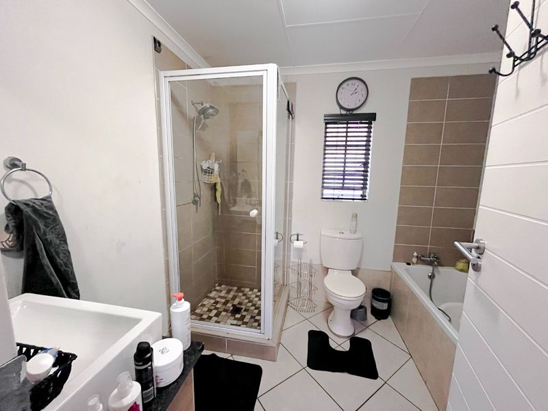 A functional bathroom featuring a separate shower enclosure, bathtub, toilet, and vanity basin with neutral tiled finishes.