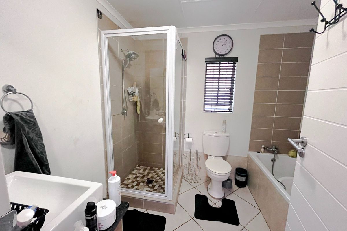 A functional bathroom featuring a separate shower enclosure, bathtub, toilet, and vanity basin with neutral tiled finishes.