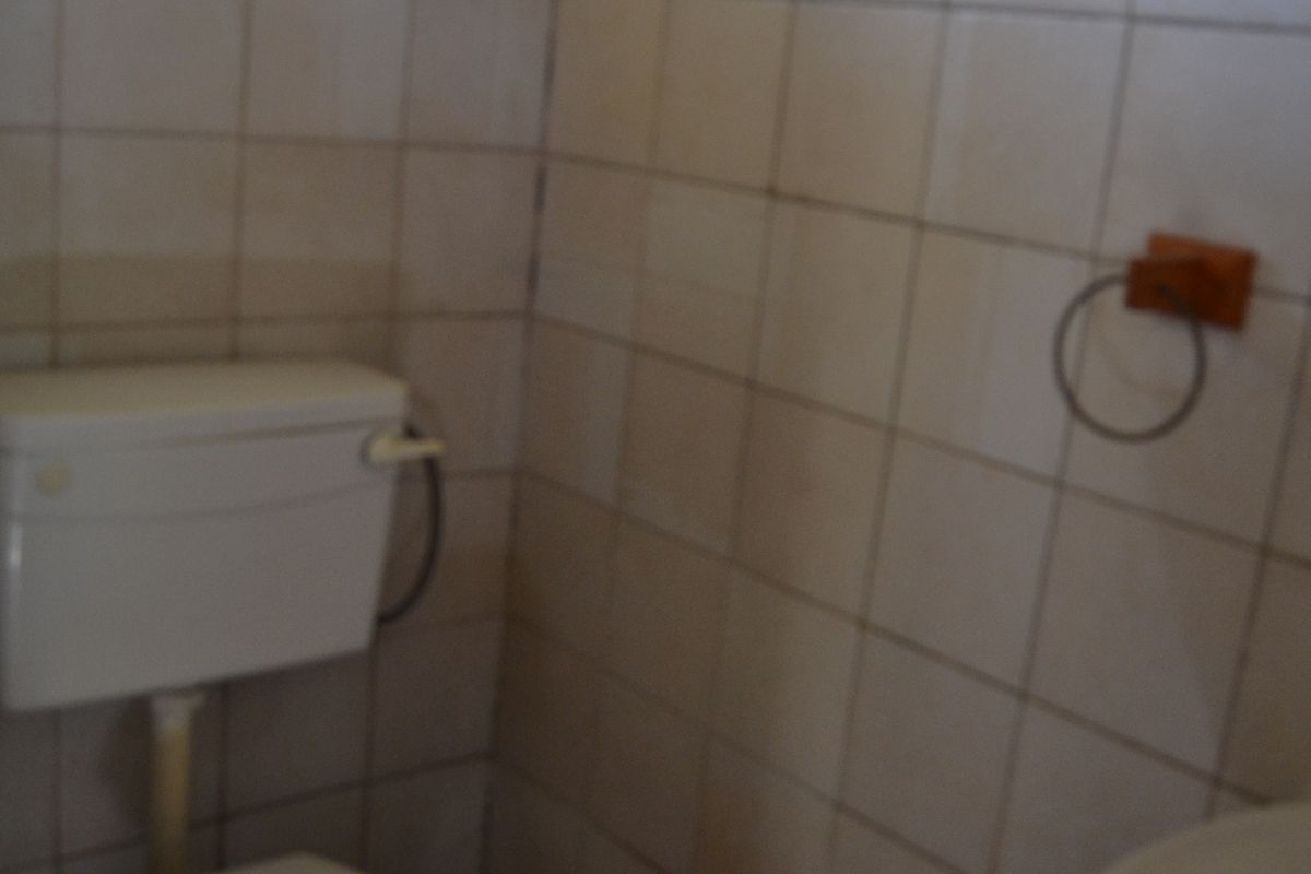 A dated bathroom featuring a standard toilet, wall-mounted washbasin, and tiled walls. The space requires cosmetic updates to improve its overall condition.