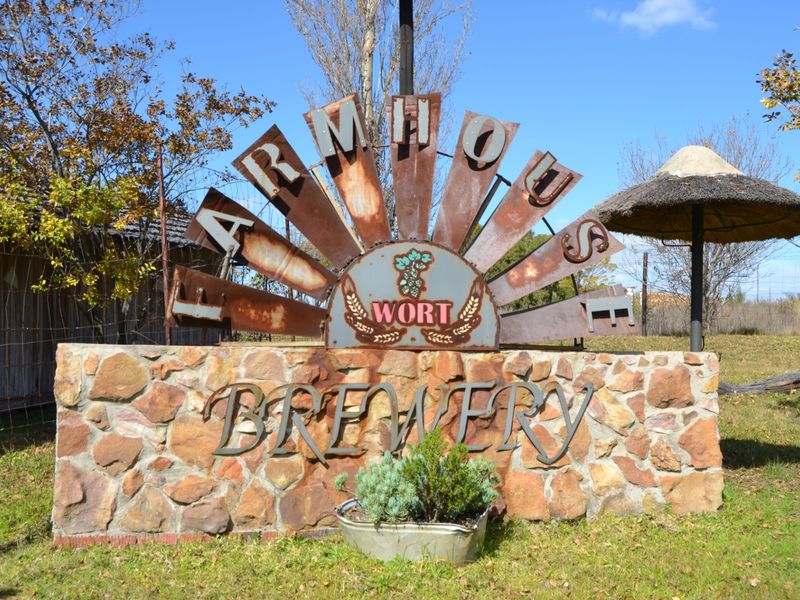 A rustic stone masonry entrance sign for the Farmhouse Brewery, featuring weathered metal lettering and a thatched shade structure.