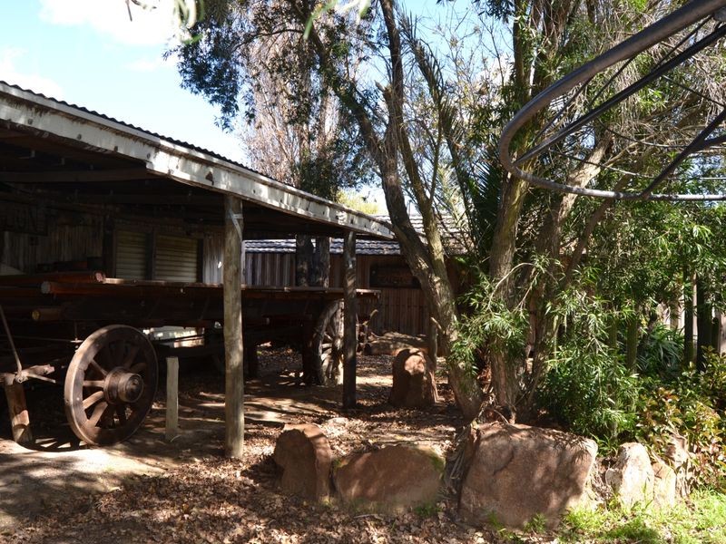 A rustic outdoor area featuring a covered timber structure with corrugated metal roofing, set within a natural garden landscape.