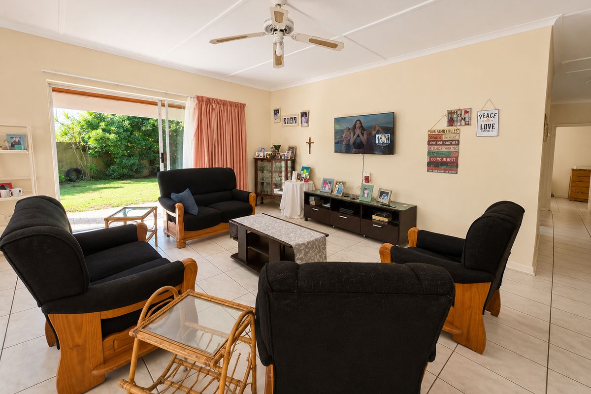 A spacious living room featuring tiled flooring, a ceiling fan, and large sliding glass doors that provide direct access to the rear garden.