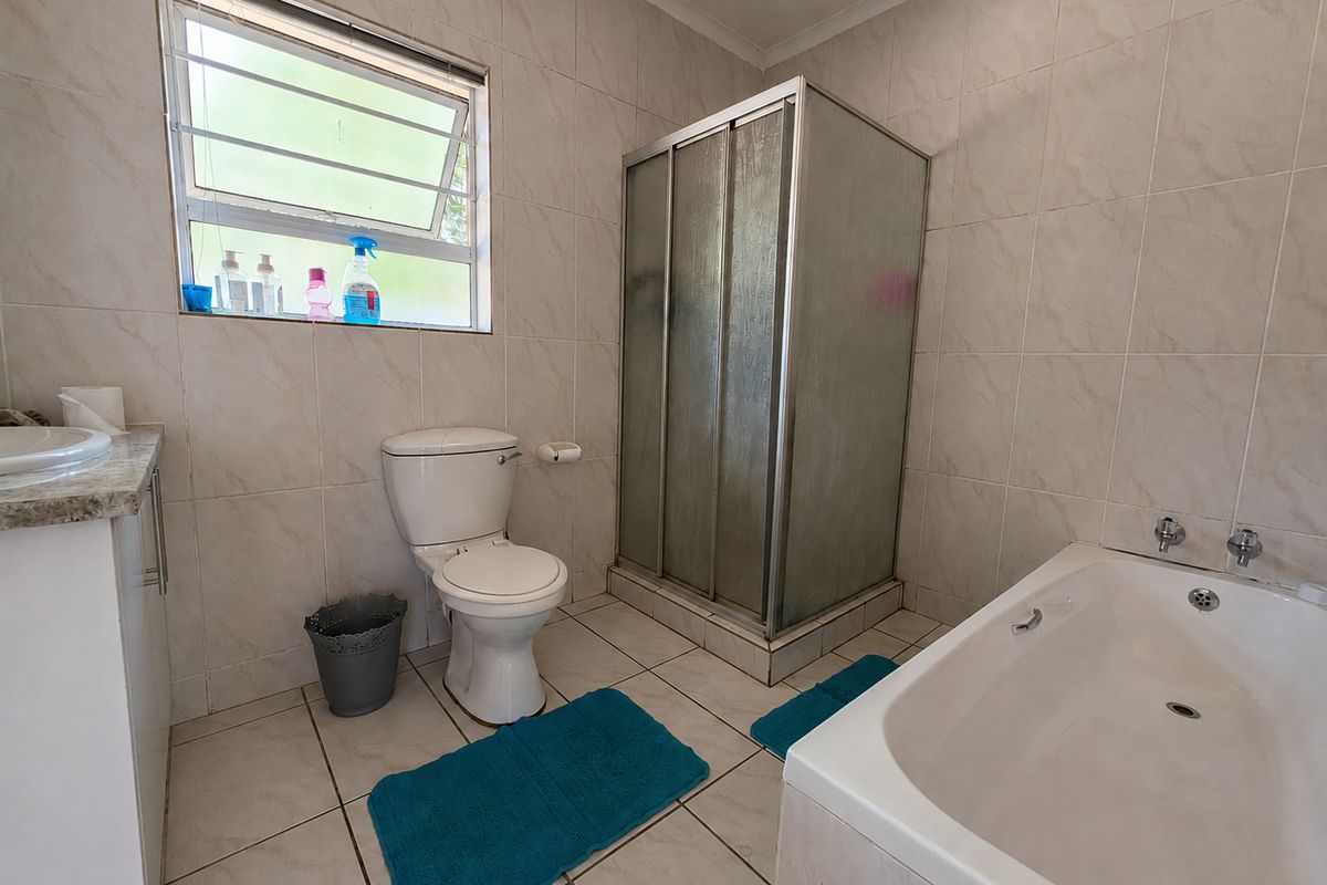 A functional bathroom featuring a shower enclosure, bathtub, toilet, and vanity basin with neutral wall and floor tiling.