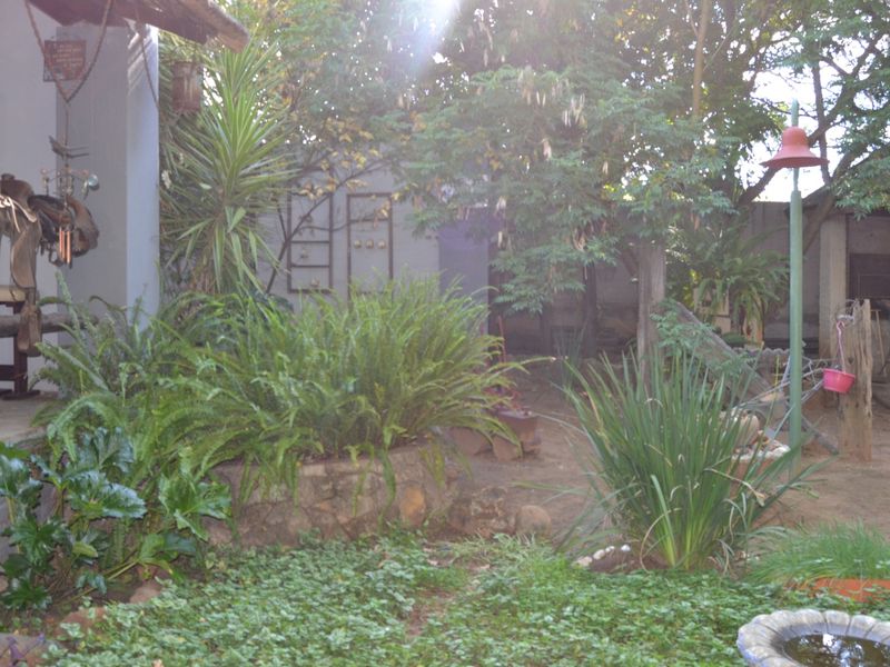 A rear garden area featuring a stone retaining wall, established greenery, and a covered patio space with a built-in braai.
