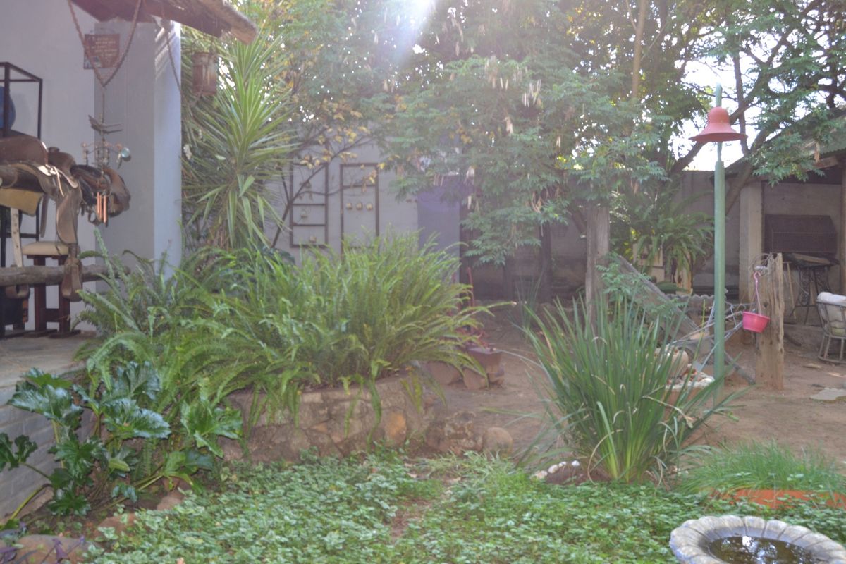 A rear garden area featuring a stone retaining wall, established greenery, and a covered patio space with a built-in braai.