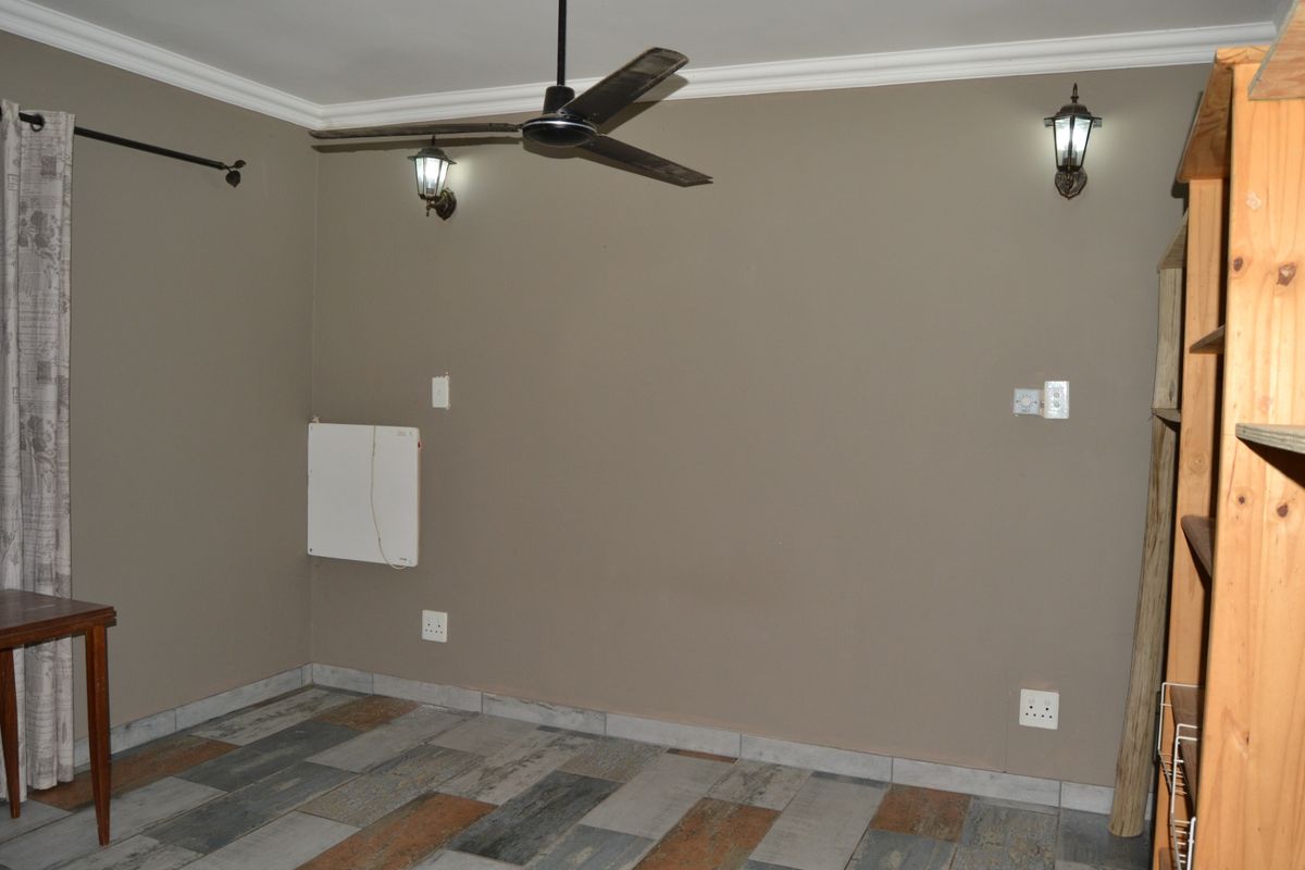 A bedroom featuring tiled flooring, a ceiling fan, wall-mounted lighting, and a wall-mounted heater, providing a functional and neutral space.