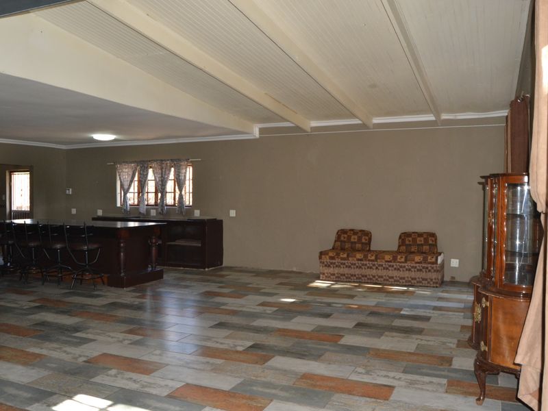 Spacious open-plan living area featuring a built-in bar counter, tiled flooring, and exposed beam ceilings, offering a versatile layout for entertaining.