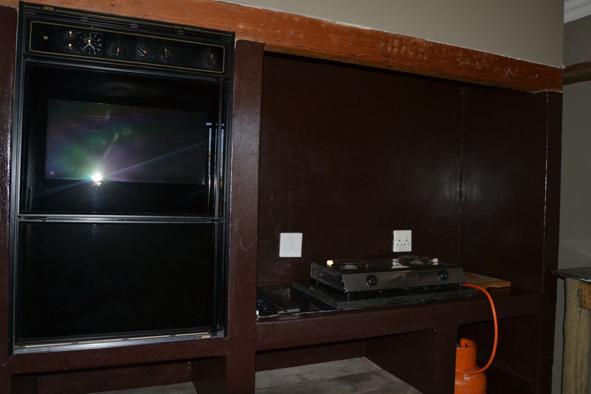A dated kitchen area featuring a built-in oven, masonry cabinetry, and a gas hob with an exposed gas cylinder.