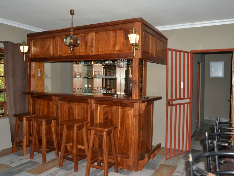 A dedicated bar area featuring a custom-built wooden bar counter with integrated mirrored shelving and overhead lighting.
