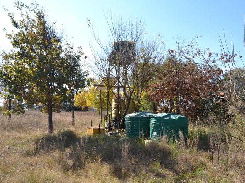 A view of the vacant land featuring established trees, water storage tanks, and a solar-powered borehole pump installation.