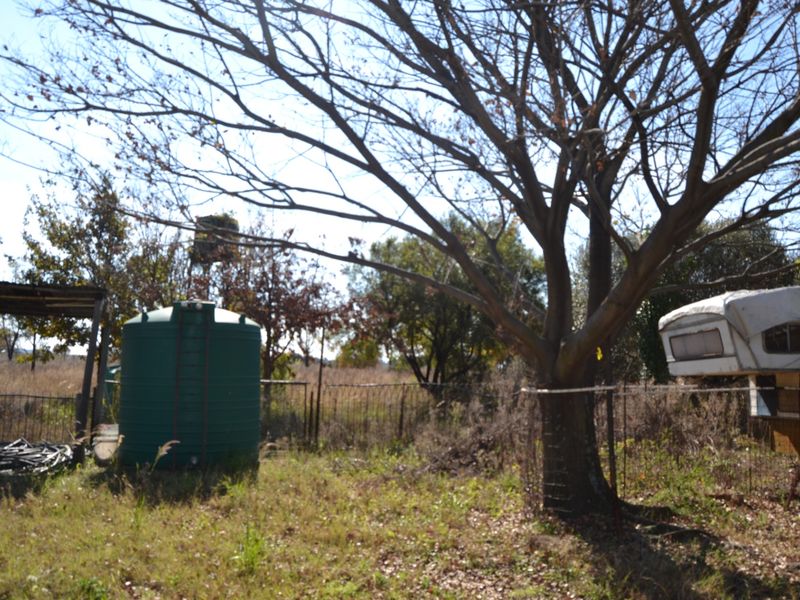 A view of the vacant residential land featuring a large water storage tank, wire fencing, and mature trees on the property.
