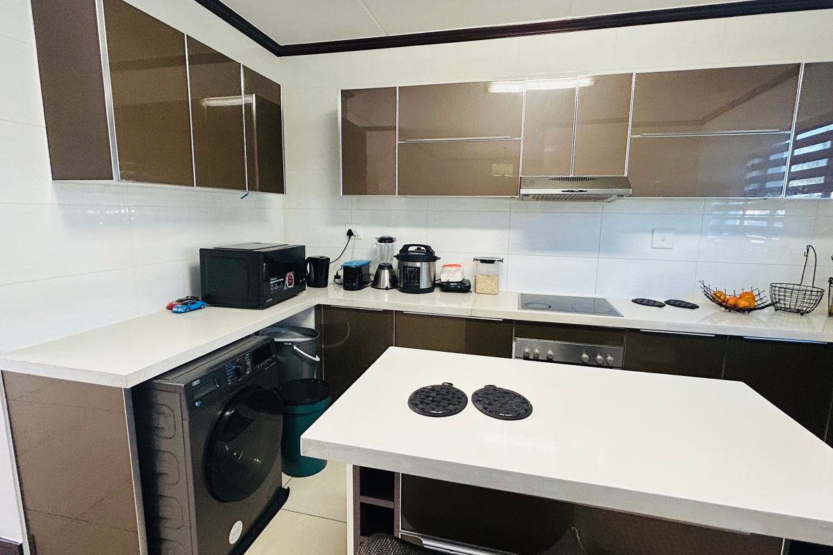 Modern kitchen featuring high-gloss brown cabinetry, white stone countertops, a central island, and integrated appliances including a hob and extractor fan.