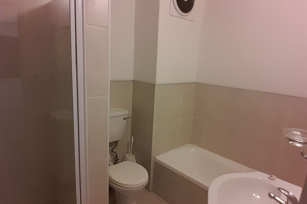 A functional bathroom featuring a shower enclosure, bathtub, pedestal basin, and toilet, with neutral wall and floor tiling.