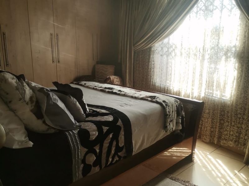 A bedroom featuring built-in wooden cupboards, tiled flooring, and natural light filtering through draped windows.