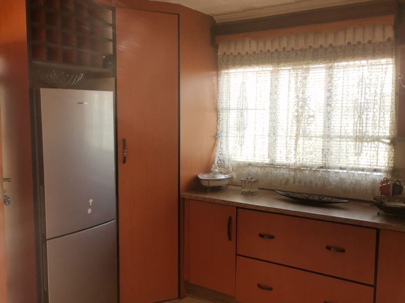 A dated kitchen featuring wood-tone cabinetry, laminate countertops, tiled flooring, and a built-in wine rack, offering potential for a modern renovation.