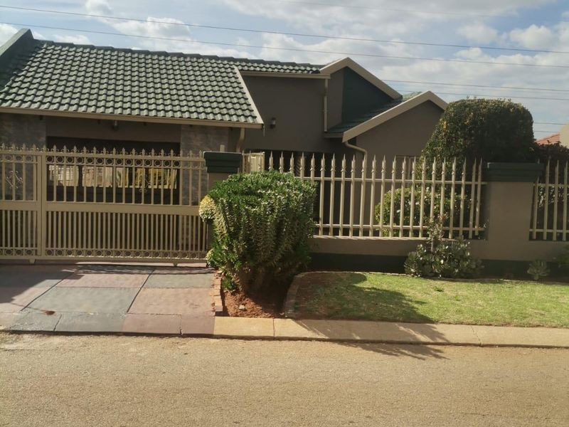 Front elevation of a residential property featuring a tiled roof, secure metal perimeter fencing, and a paved driveway entrance.
