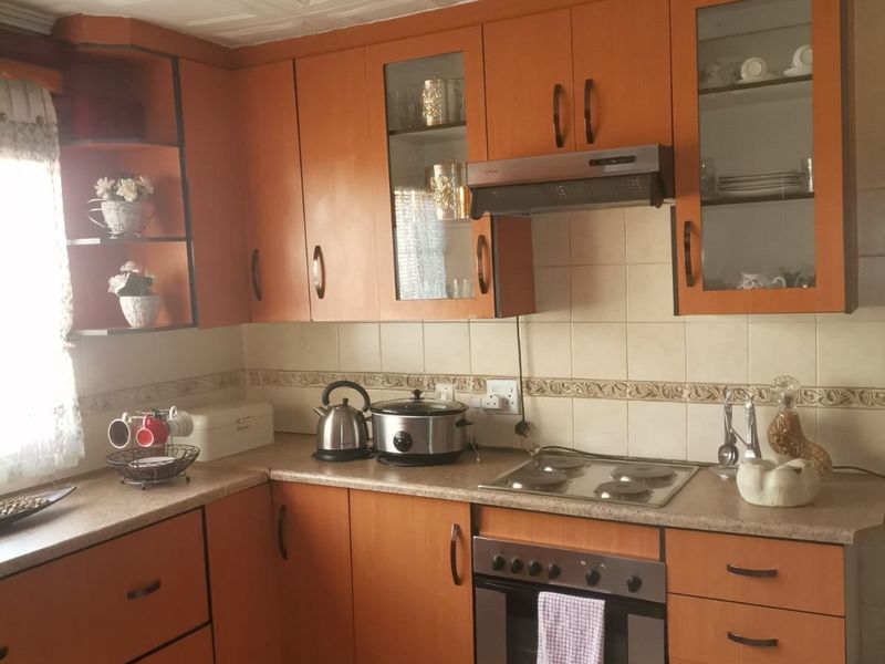A functional kitchen featuring wood-tone cabinetry, built-in oven with electric hob, tiled backsplash, and decorative ceiling tiles.