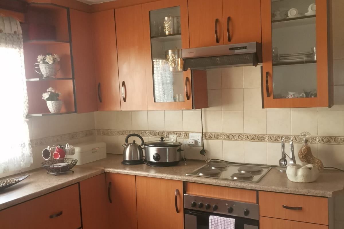 A functional kitchen featuring wood-tone cabinetry, built-in oven with electric hob, tiled backsplash, and decorative ceiling tiles.
