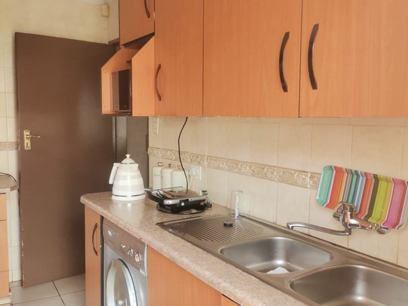 A functional kitchen featuring laminate cabinetry, a double bowl stainless steel sink, tiled backsplash, and dedicated space for a washing machine.